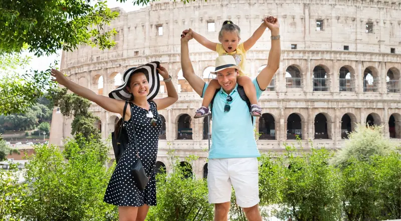 Father with daughter on his shoulders and mother, arms raised in front of the Colosseum